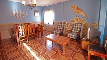 Una sala de estar con un comedor de madera, dos sillones, una mesa de centro, un televisor y una pared de piedra con un mural de aves.