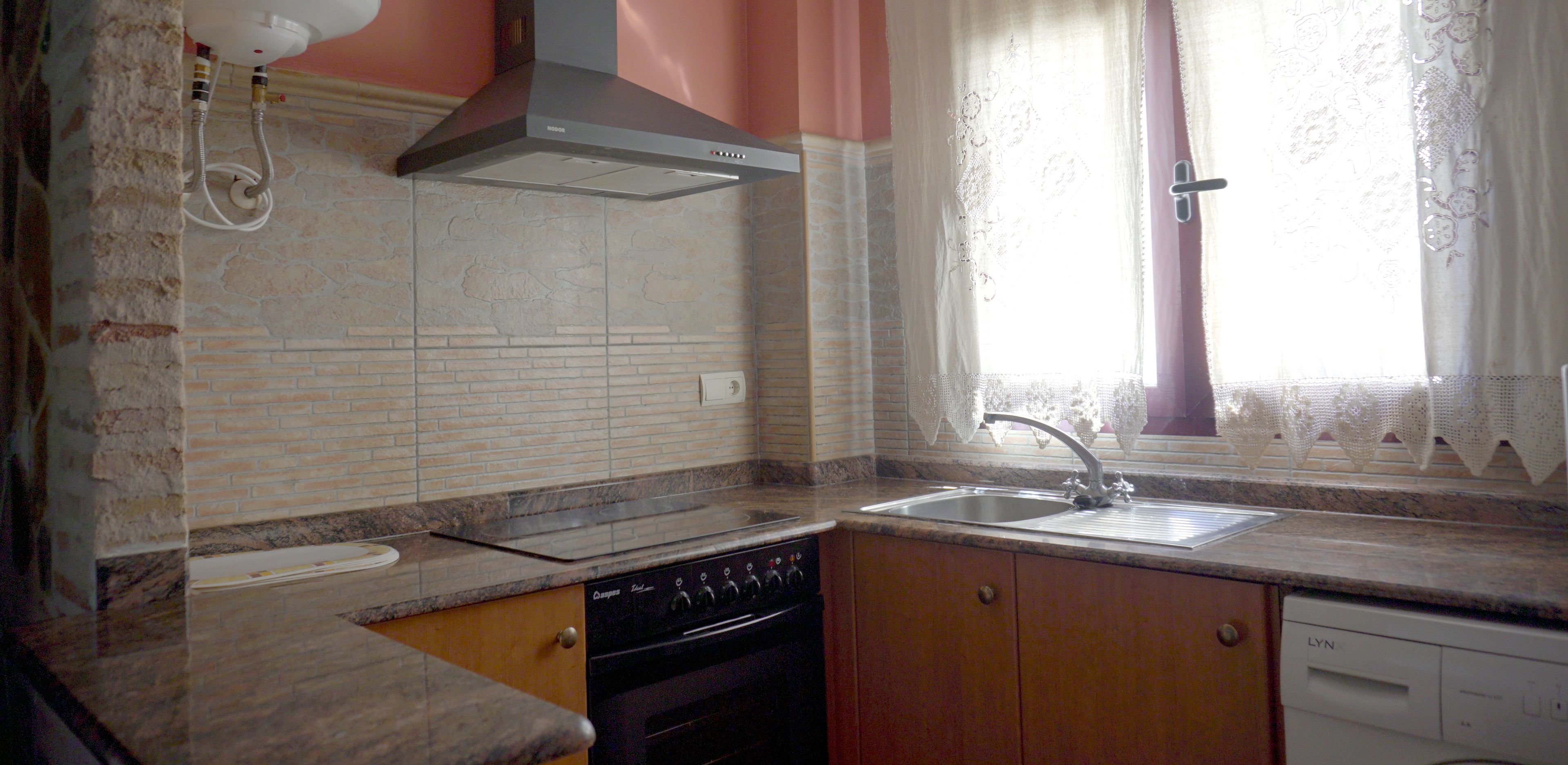 Una cocina con estufa, lavavajillas y una ventana con cortinas de encaje.