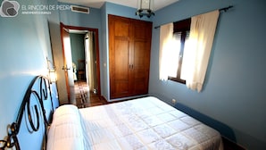 A bedroom with a bed, wooden wardrobe, and a window with curtains. - El Rincón de Piedra Apartamentos Rurales (Enguidanos)