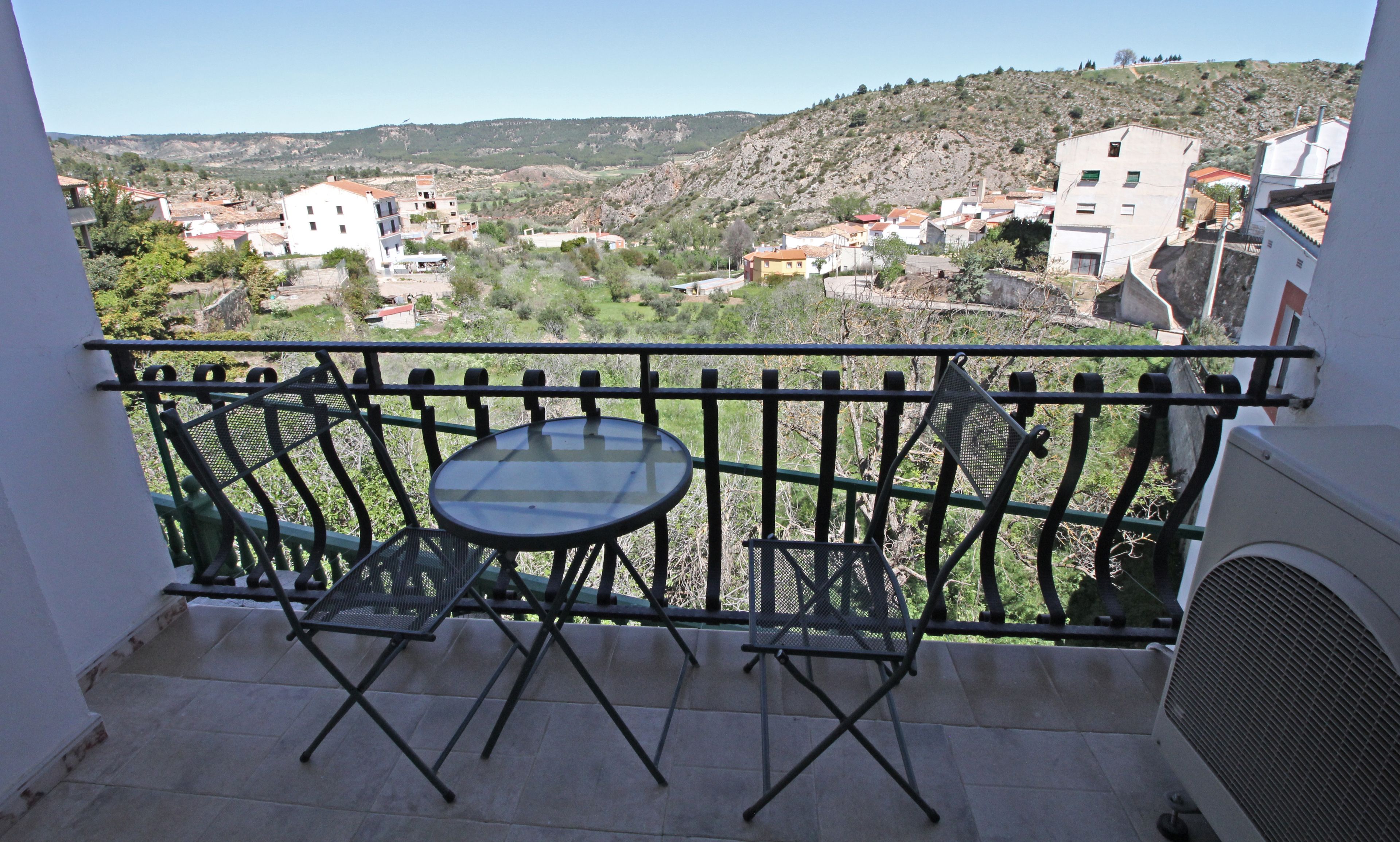 Un balcon avec une table et des chaises, donnant sur une colline parsemée de bâtiments.