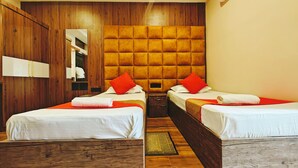 A hotel room with two beds, wooden headboards, a large mirror, and a wooden floor. - Hotel Nakshatra (Dima Hasao)