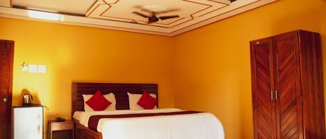 A hotel room with a bed, a wardrobe, a desk, and a ceiling fan.