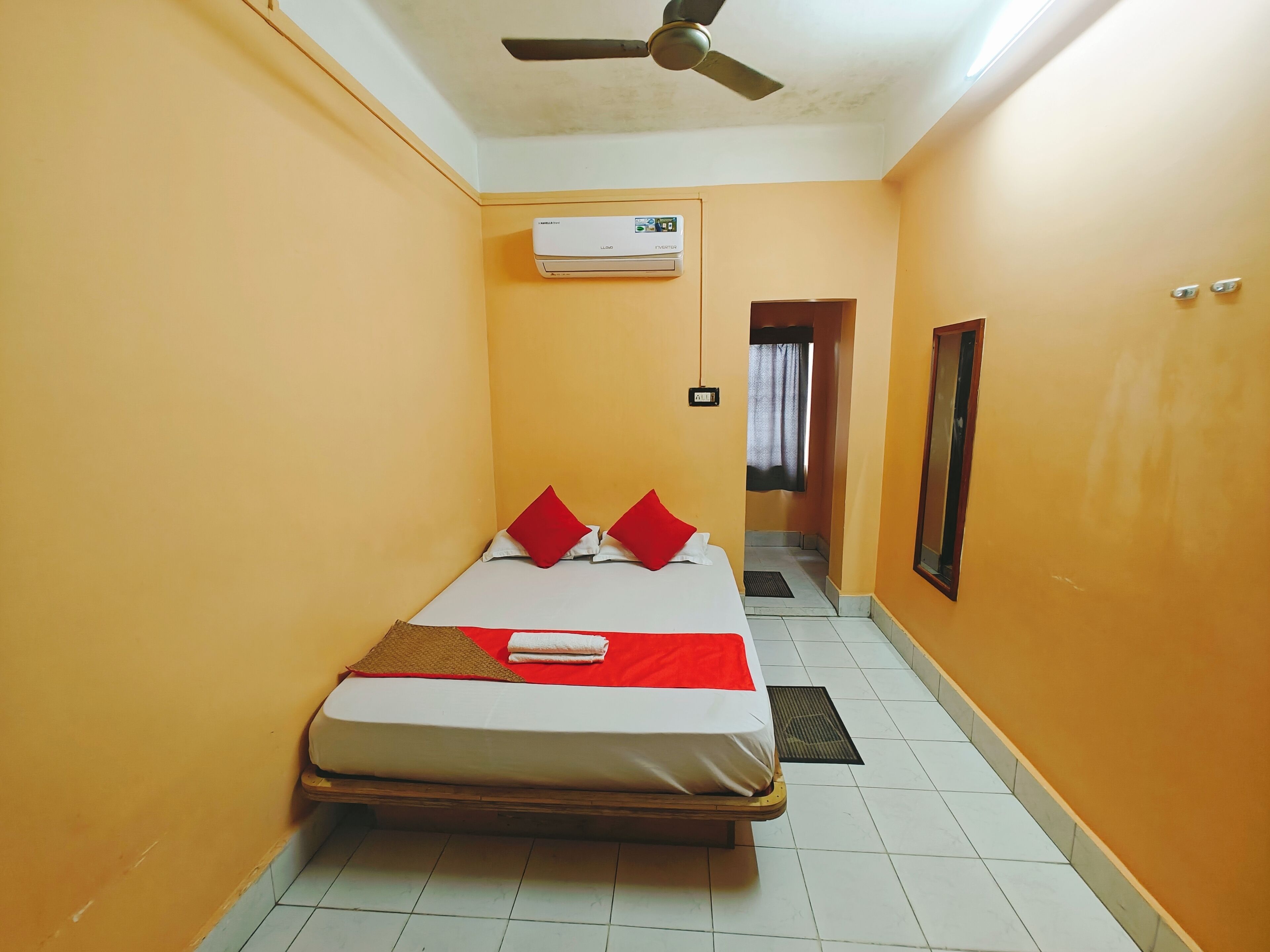 A narrow hotel room with a bed, a ceiling fan, and an air conditioning unit.
