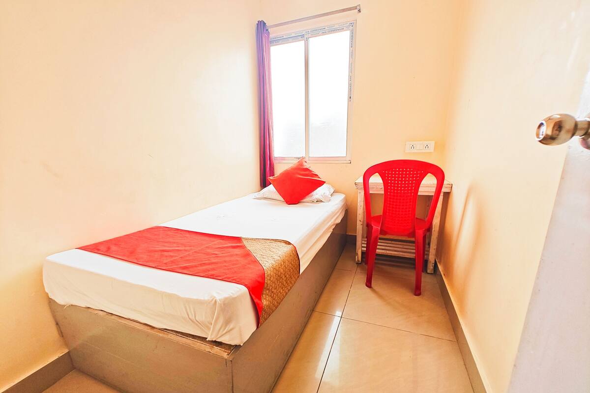 A small, single-bed room with a red chair and a window with curtains.