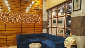 A modern living room with a blue sectional sofa, a round wooden coffee table, and a decorative lamp. - Hotel Nakshatra (Dima Hasao)
