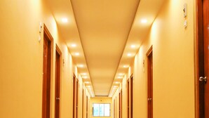 A long, well-lit hallway with wooden doors on both sides, leading to rooms. - Hotel Nakshatra (Dima Hasao)