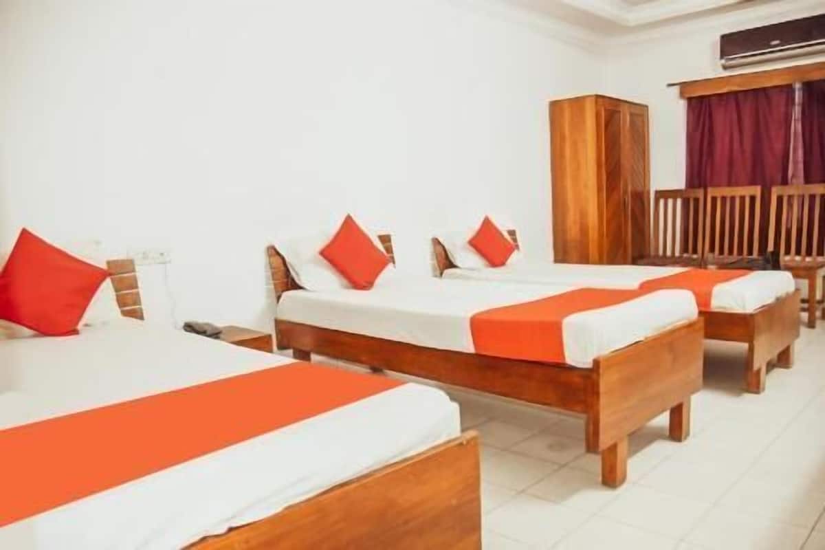 A hotel room with three wooden beds, each with white bedding and orange accents, a wooden wardrobe, and a red curtain.