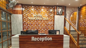A reception desk with a wooden finish and a marble floor. - Hotel Nakshatra (Dima Hasao)