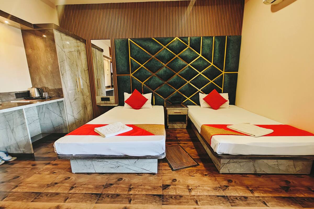 A hotel room with two single beds, a small kitchenette, and a large mirror.