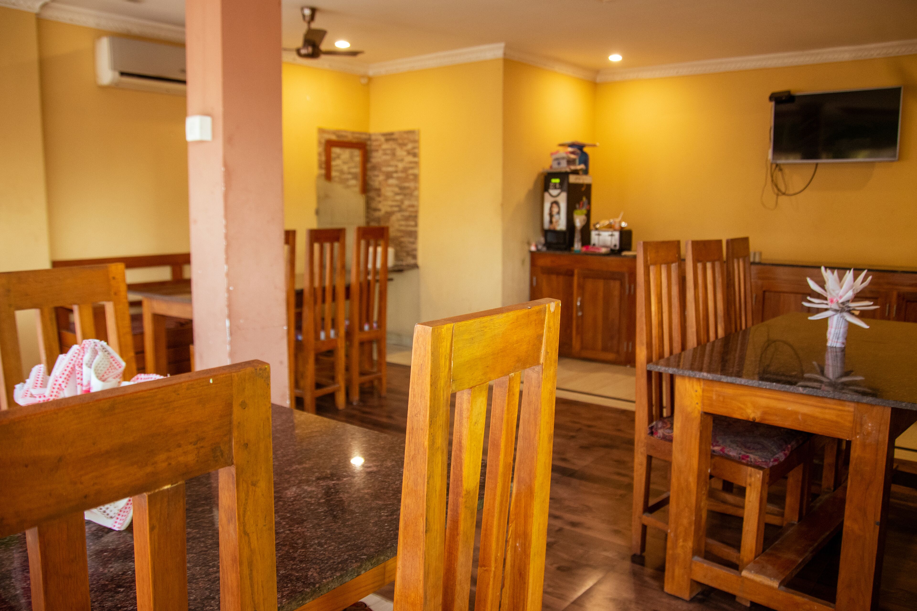Un comedor con sillas de madera y una mesa de vidrio, con una pared de piedra y un televisor montado.