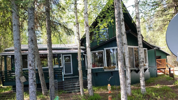 Eine rustikale Holzhütte, umgeben von hohen Bäumen, mit einem eingezäunten Hof und einem kleinen Garten.