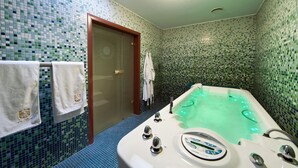 A bathroom with a green-tiled wall, a glass shower door, a white bathtub with a control panel, and two white towels on a rack. - Willa Różana - Ormonde Resorts (Naleczow)