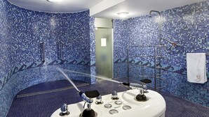 A bathroom with a blue mosaic tile wall, a white sink with multiple faucets, a handheld showerhead, and a towel hanging on a rack. - Willa Różana - Ormonde Resorts (Naleczow)