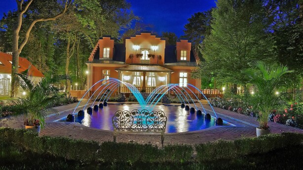 A hotel with a pool and fountain, surrounded by trees and well-lit pathways. - Willa Różana - Ormonde Resorts (Naleczow)
