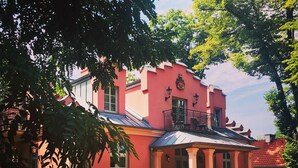 A pink building with a balcony, surrounded by well-maintained gardens and a paved courtyard. - Willa Różana - Ormonde Resorts (Naleczow)
