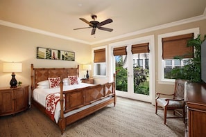 A bedroom with a four-poster bed, a ceiling fan, a large window with a view, and a wooden nightstand.