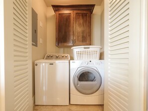 A laundry room with a front-loading washer and dryer, wooden cabinets, and a laundry basket.
