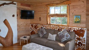 Acogedor interior de cabaña con sofá, televisor y ventana con vistas a la vegetación.