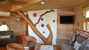 Interior acogedor de una cabaña con un cuadro de pared de árbol de madera, un televisor de pantalla plana, un sofá y una silla.