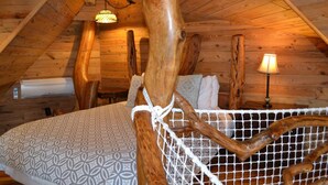 Un dormitorio acogedor en el ático, con una cama, una lámpara colgante y techo de madera.