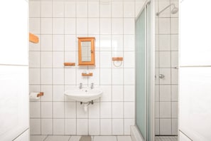 Une salle de bain avec des carreaux blancs, un lavabo, un miroir et une douche.