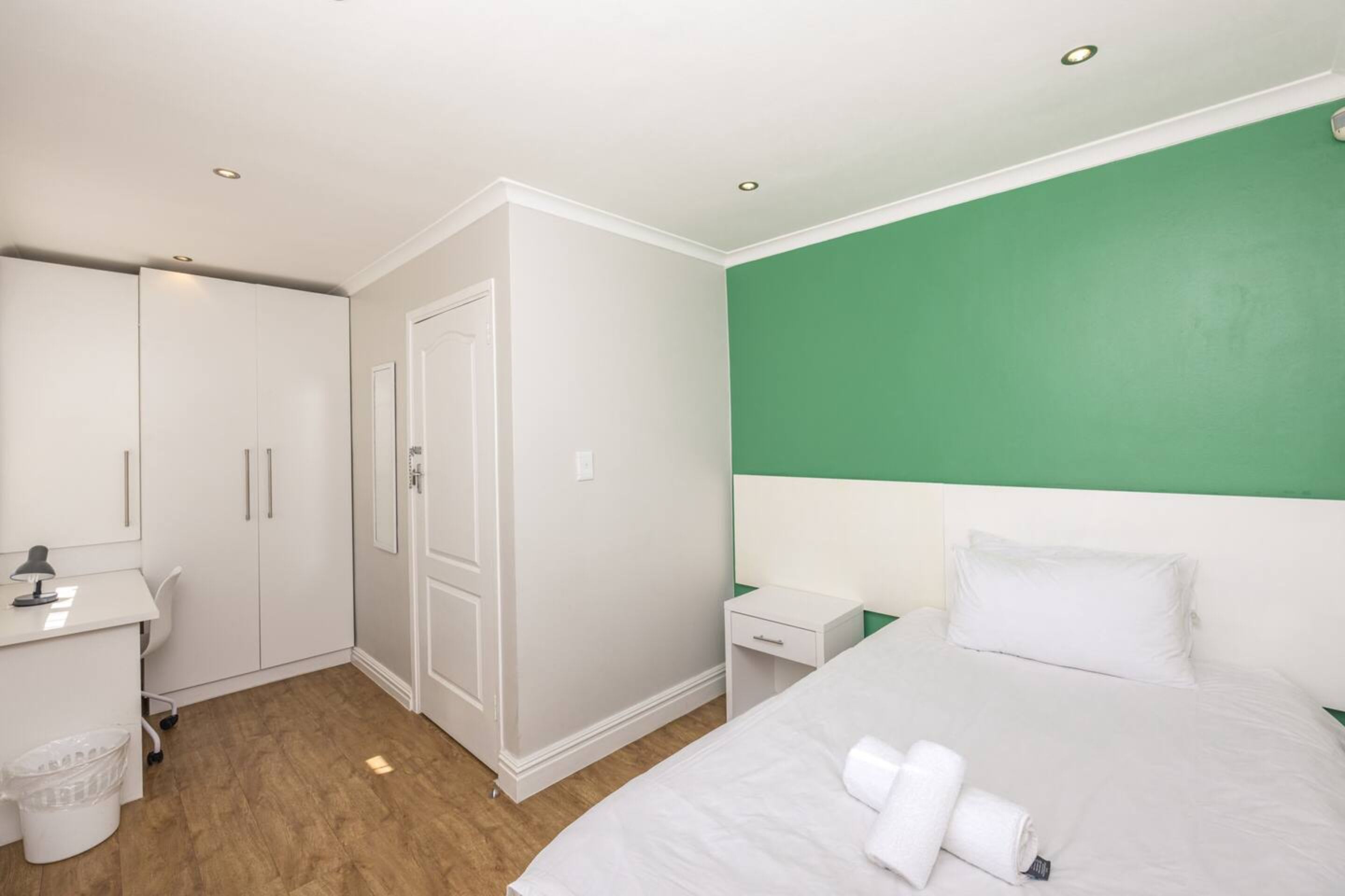 Une chambre d’hôtel comprenant un lit, un bureau, une chaise, une armoire et un mur d’accent de couleur verte.