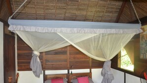 A bed with a wooden headboard, white mosquito netting, and two pillows. - Boraha Village (Nosy Boraha)