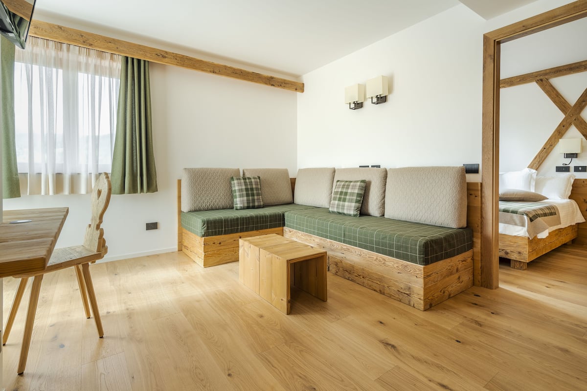 A cozy room with a wooden floor, a green sofa with plaid cushions, a wooden coffee table, and a wooden-framed bed.
