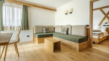 A cozy room with a wooden floor, a green sofa with plaid cushions, a wooden coffee table, and a wooden-framed bed.