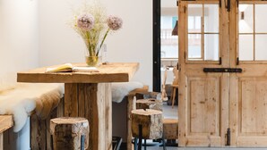 A modern interior with a wooden bar area, bar stools, and a vase with flowers. - Camina Suite & Spa (Cortina d'Ampezzo)