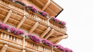 A multi-story building with wooden balconies adorned with pink flowers. - Camina Suite & Spa (Cortina d'Ampezzo)
