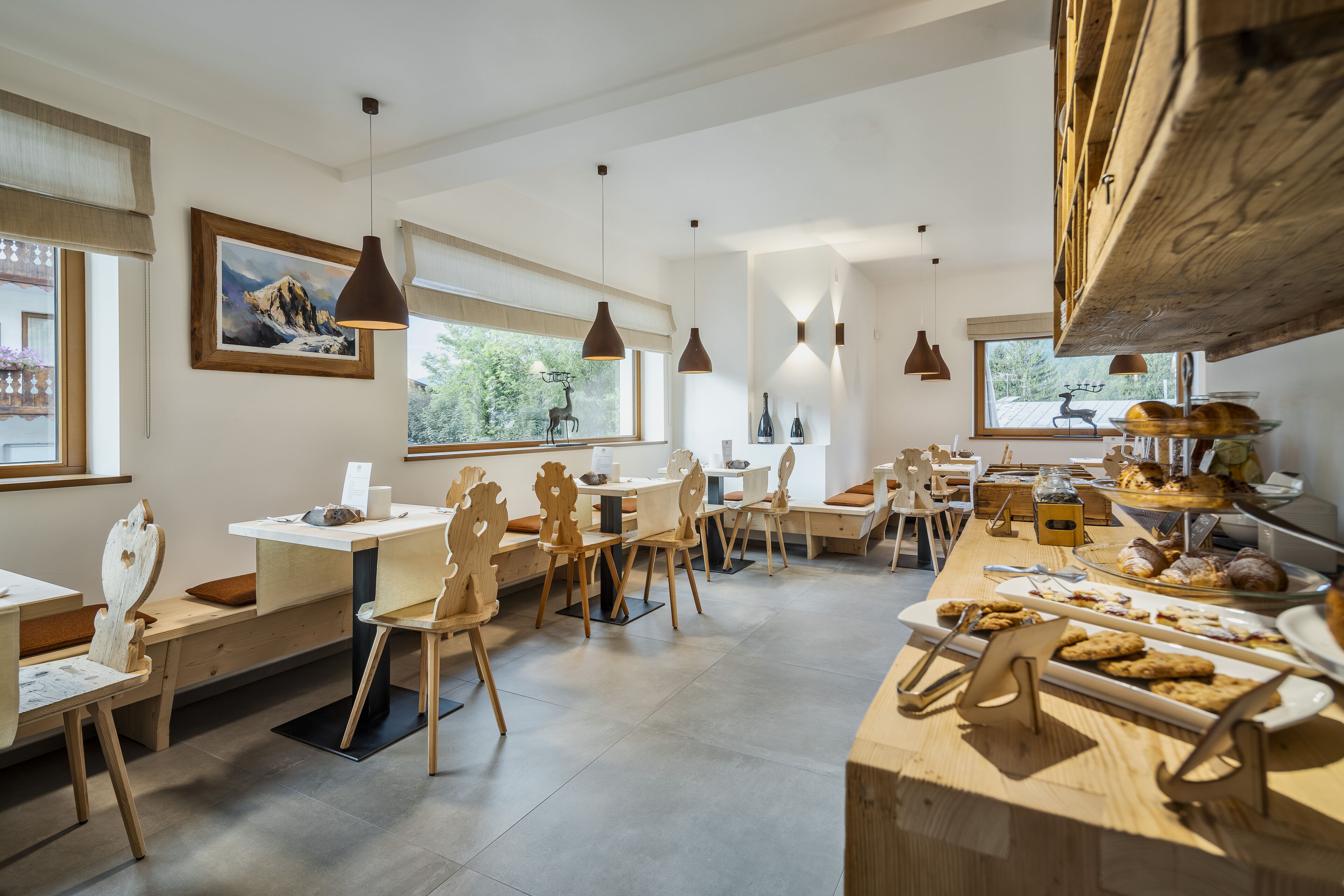A modern dining area with wooden furniture, pendant lighting, and a buffet with pastries.