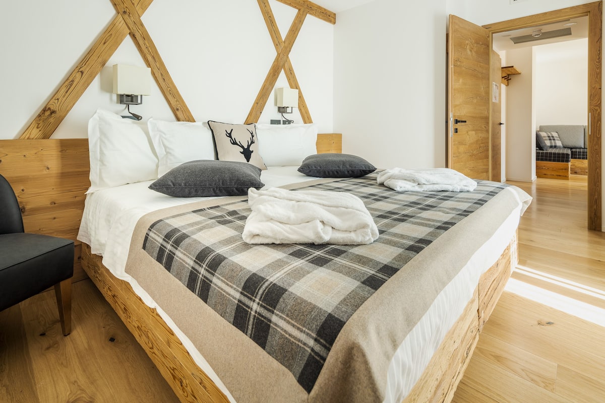 A bedroom with a wooden bed frame, a plaid bedspread, and a black chair.