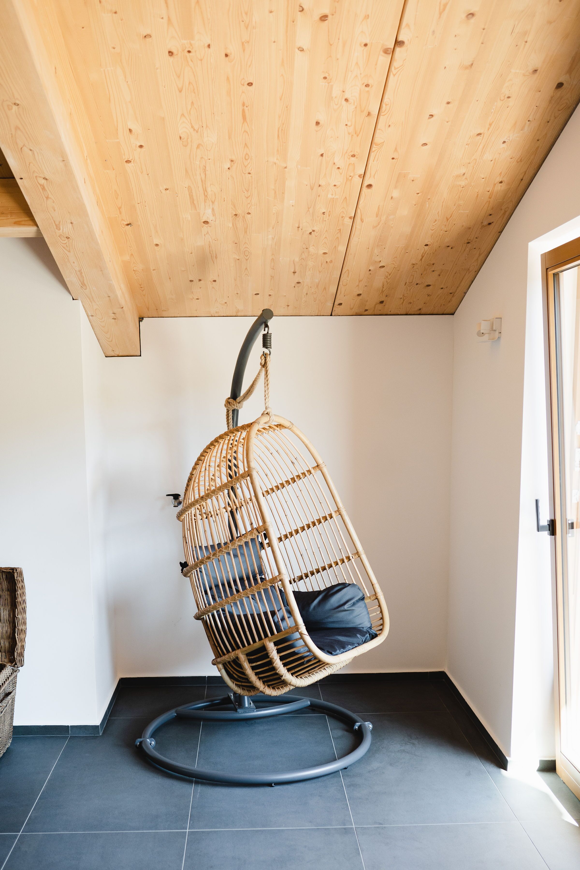 A room with a wooden ceiling, a hanging chair, and a dark tiled floor.