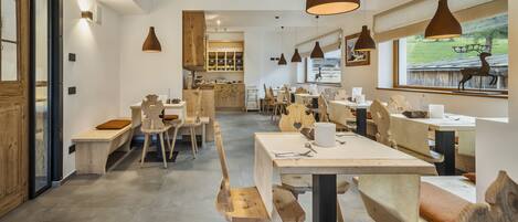 En restaurantindretning med træmøbler, hængende lamper og udsigt til det fri.