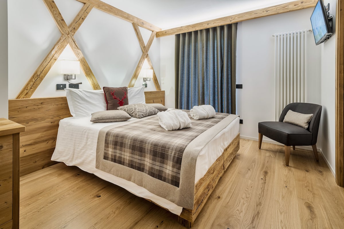 A bedroom with a wooden bed, a chair, and a TV on the wall.