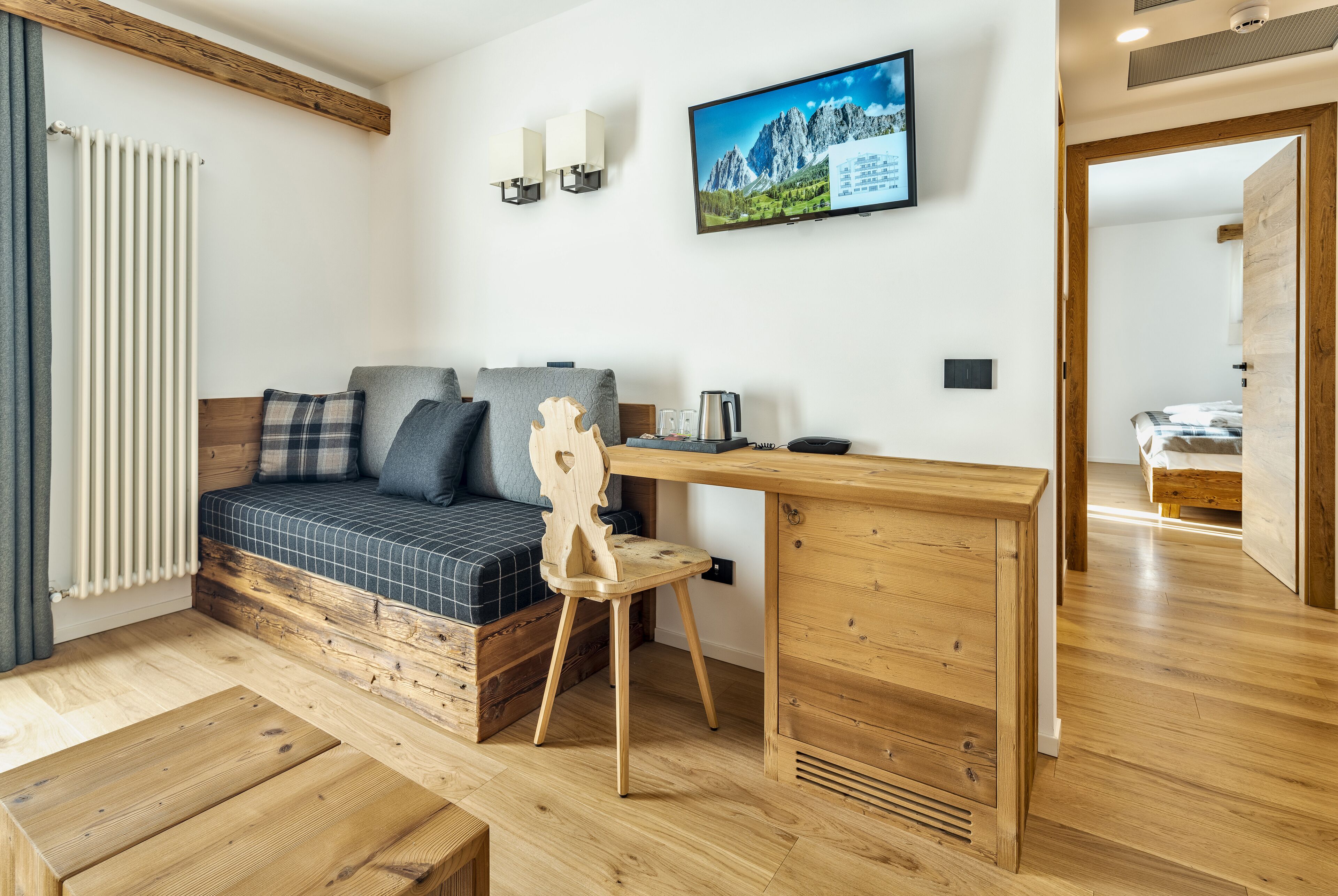A cozy room with a bed, a wooden desk, a chair, and a TV on the wall.