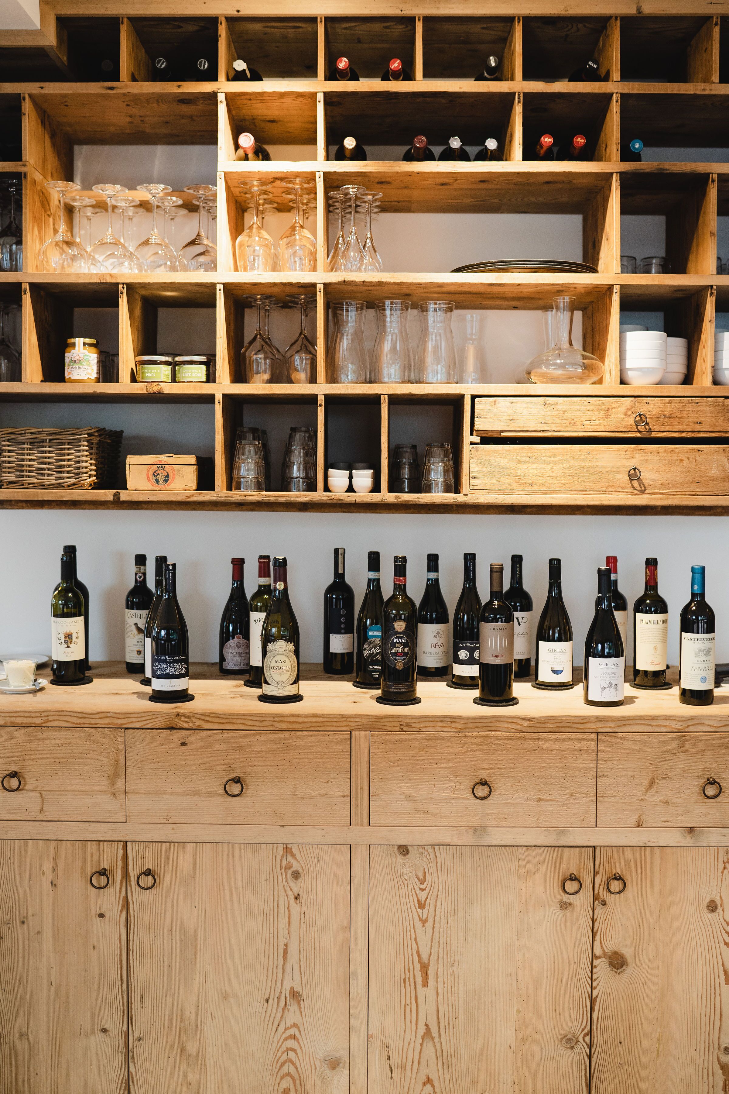 A wine cellar with wooden shelves and drawers, containing various wine bottles and glassware.