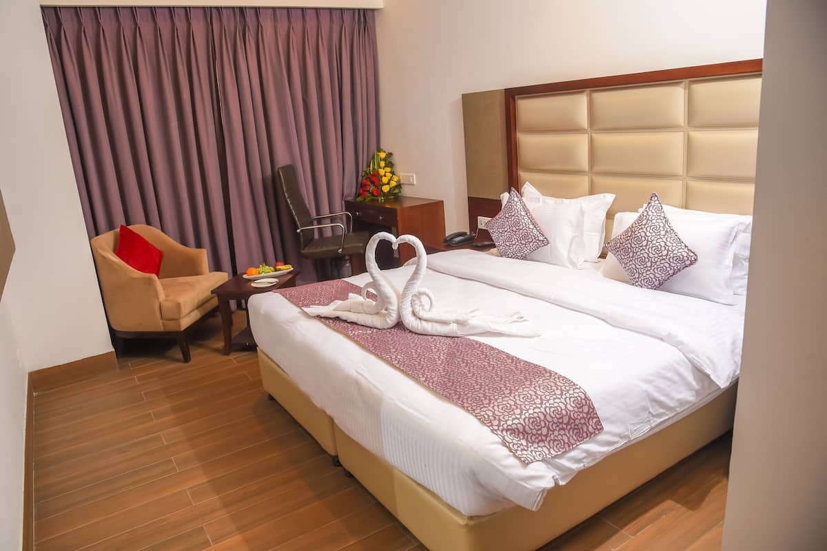 A hotel room with a large bed, a chair, a desk with a phone, and a vase of flowers.