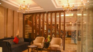 A lobby with a sofa, armchairs, a coffee table, a chandelier, and a staircase in the background. - Bharawan Clarks Inn Express (Amritsar)