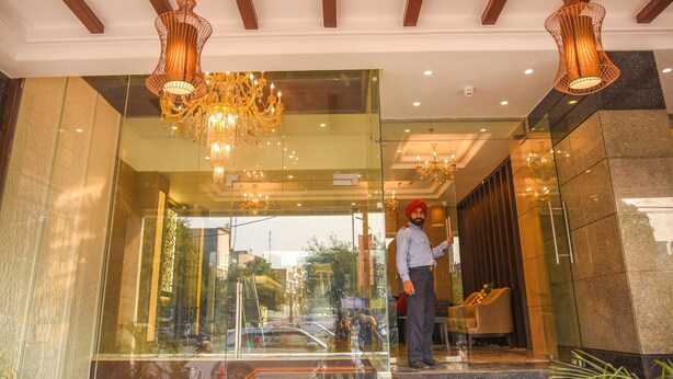 A hotel lobby with a glass entrance, chandeliers, and a security guard. - Bharawan Clarks Inn Express (Amritsar)