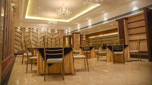 A spacious banquet hall with gold chairs and tables, elegant chandeliers, and a modern ceiling design. - Bharawan Clarks Inn Express (Amritsar)