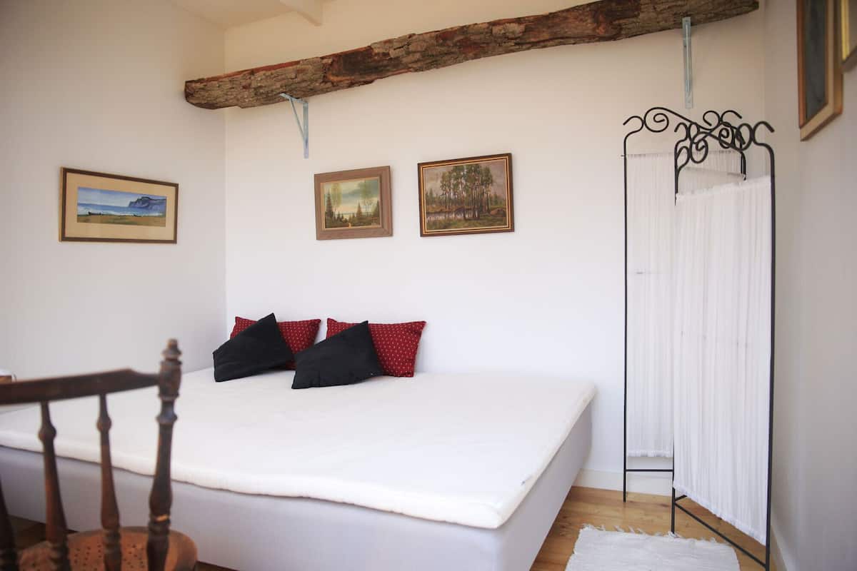 A bedroom with a large bed, a wooden chair, a metal bed frame, and three framed pictures on the wall.