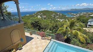 Une piscine avec vue sur un paysage côtier, un balcon avec une balustrade et un bâtiment avec une porte.