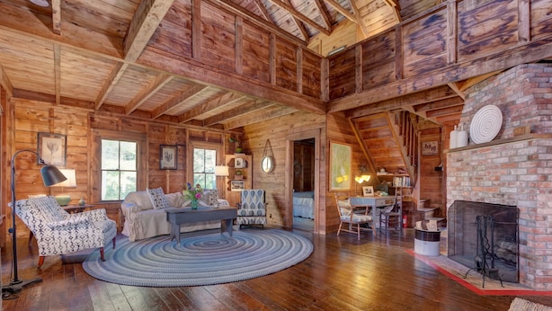 A rustic cabin interior with a wooden floor, a fireplace, and a cozy seating area with a round rug. - Charming lakefront cabin close to Acadia National Park (Franklin)
