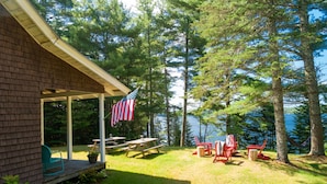 A covered patio with picnic tables and chairs, an American flag, and a view of a lake surrounded by trees. - Charming lakefront cabin close to Acadia National Park (Franklin)