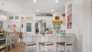 A kitchen with white cabinets, a stainless steel refrigerator, and a dining area with white chairs and a wooden table. - 5BR Home. PRIVATE Pool. Cherry Grove, Sleeps 13 (North Myrtle Beach)