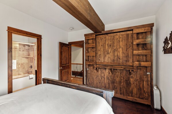 Een slaapkamer met een groot bed, een houten garderobe en een badkamer die door een open deur zichtbaar is.