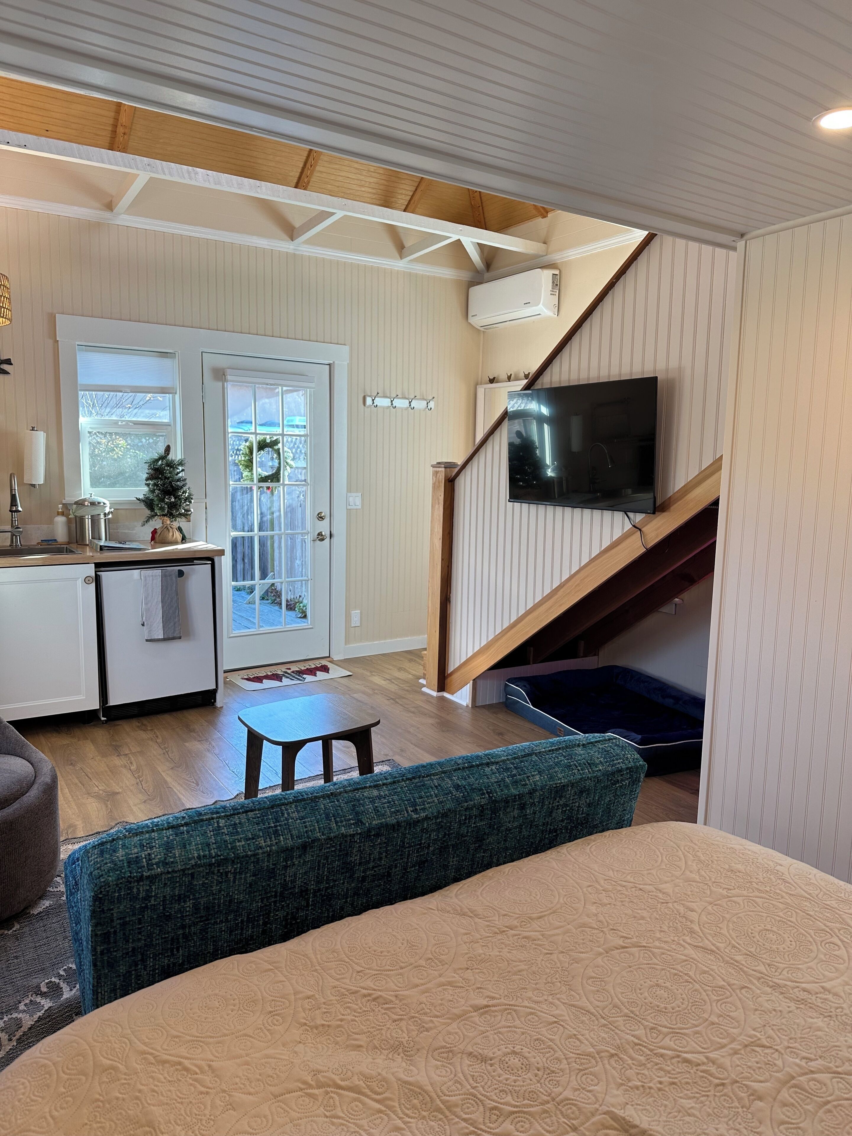 A room with a bed, a TV mounted on the wall, a staircase, and a small kitchenette.