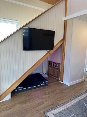 A staircase with a flat-screen TV mounted on the wall, a baby gate at the bottom, and a patterned rug on the floor. - Small Beach Cottage near the Coastal Trail and The Ritz (Half Moon Bay)